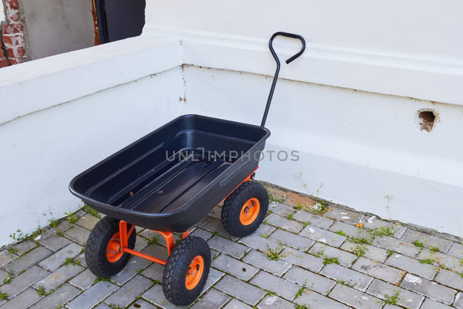 Photo a four-wheeled garden wheelbarrow empty against the background of a house wall. Tools and devices. Country life. The countryside.