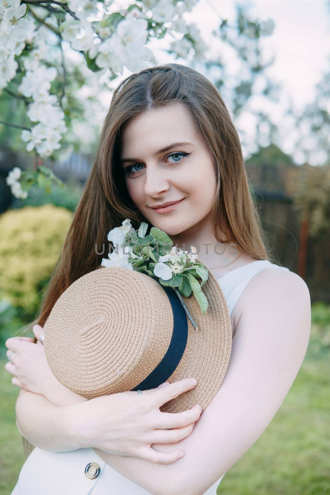 Beautiful young girl in white dress and hat in blooming Apple orchard. Blooming Apple trees with white flowers. by Annu1tochka