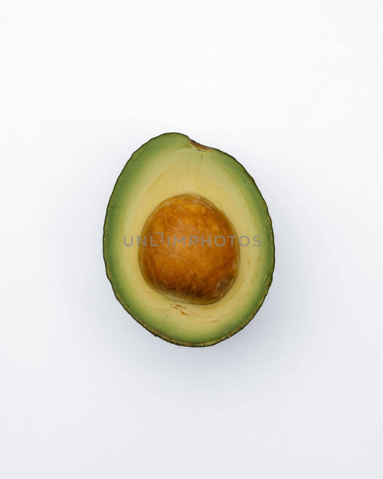 A cut avocado with its seed intact, presented on a stark white background to highlight its vibrant green color