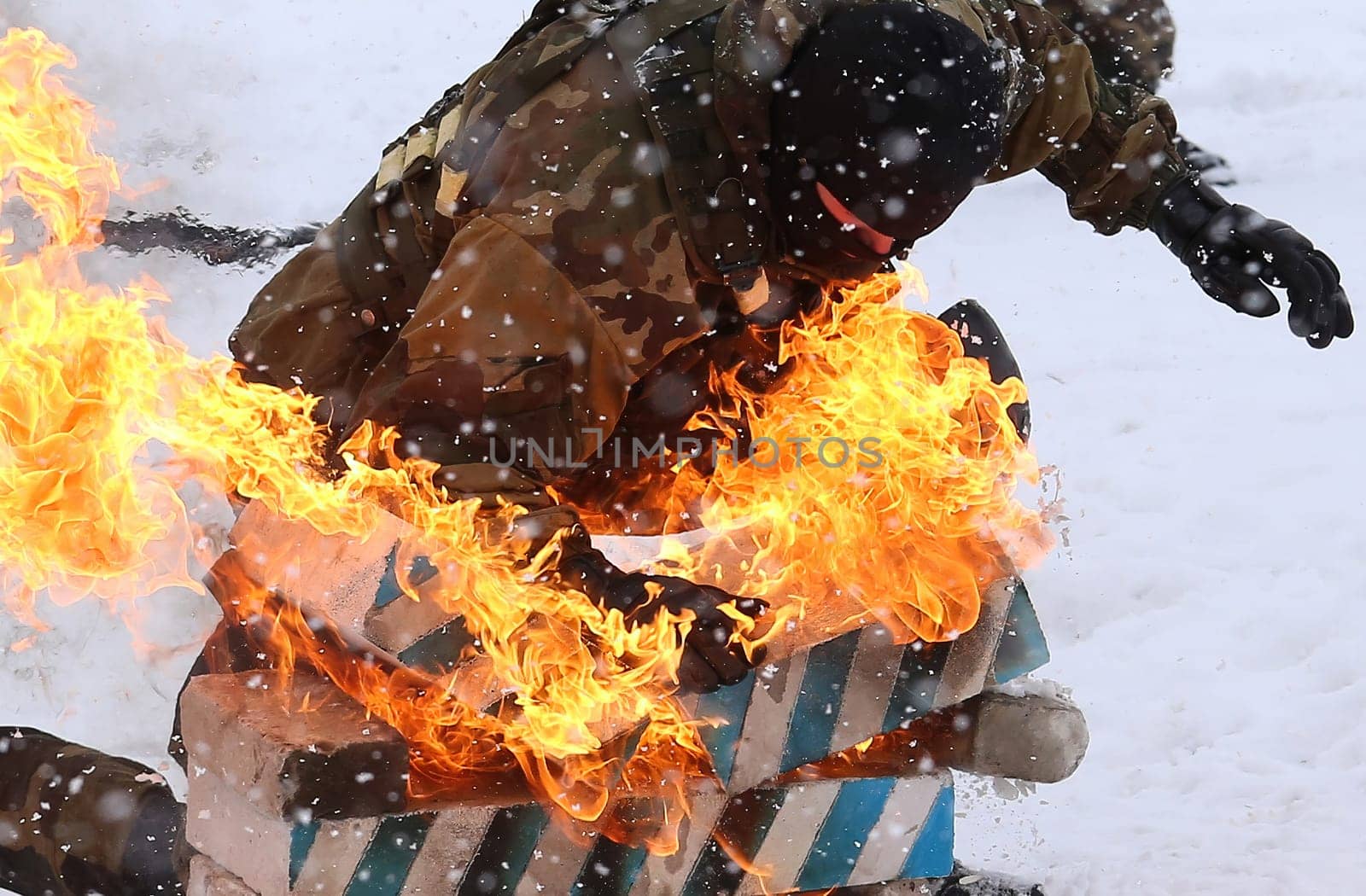 A commando in protective gear fearlessly slides down a snowy slope on a rescue sled, surrounded by flames and smoke, demonstrating courage and skill in this captivating image.