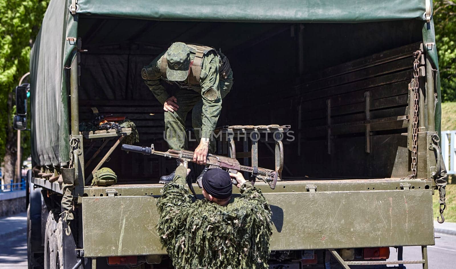 Soldiers unload firearms from a military truck. A soldier in the back of a truck.