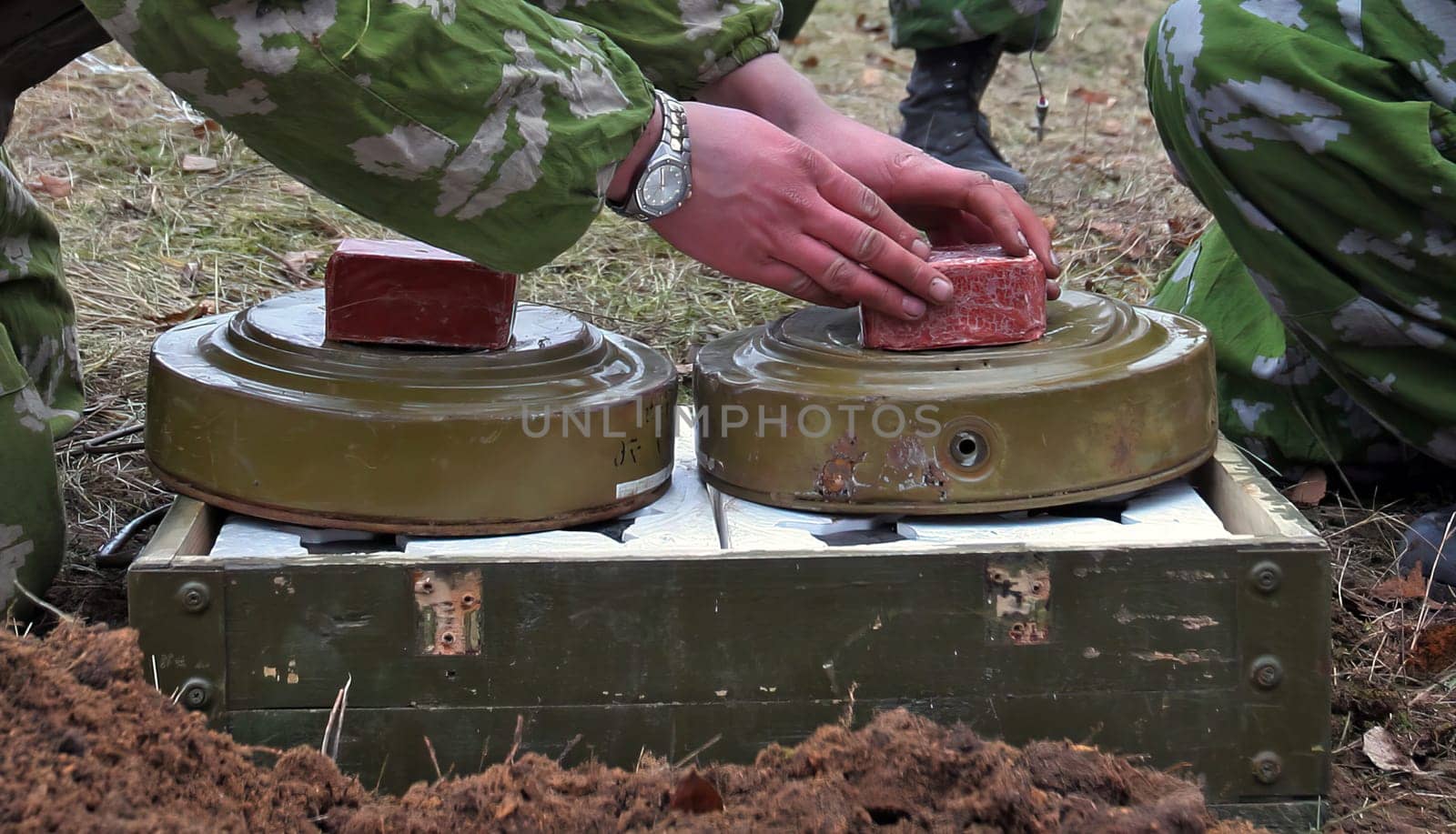 Soldiers in camouflage planting land mines in a war-torn field. Strategic placements deter enemy. Focused soldiers seen from a low angle with rifles. Portrays the gravity of military defense.