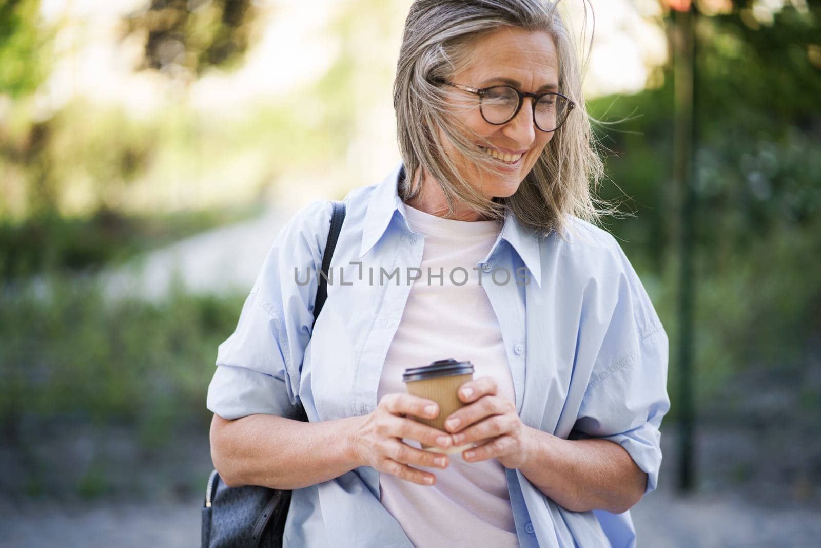 A woman wearing glasses is focused on her cup of coffee, absorbed in what she is drinking.