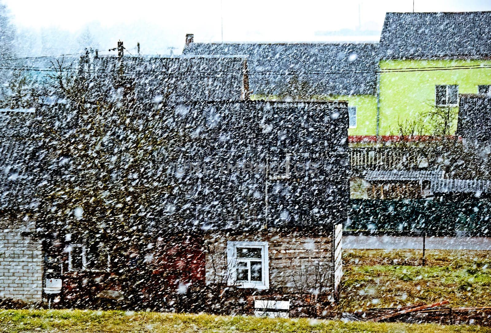 The image shows a small village on a gloomy winter day. The snow is falling heavily, and the houses are covered in snow. The image has a cold and desolate feel to it.