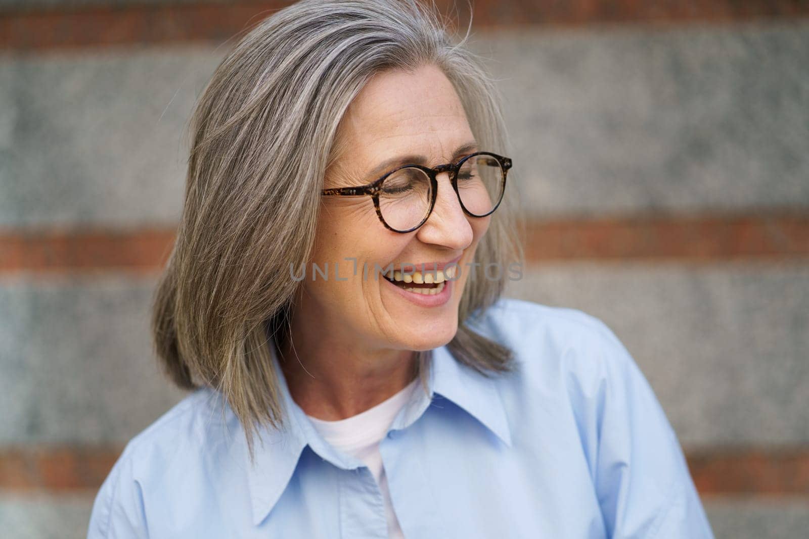 Happy Older Woman Wearing Glasses and Blue Shirt by LipikStockMedia