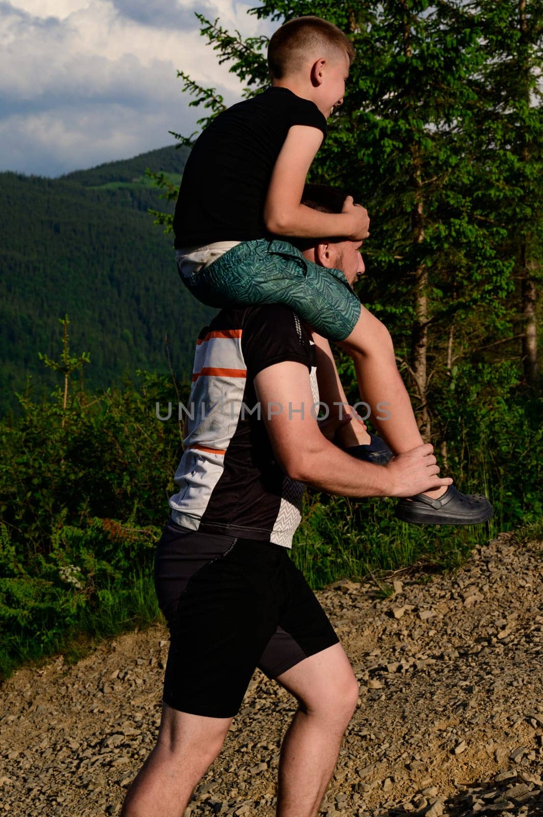 dad carries his son on his shoulders on the background of the mountains, active recreation in the mountains during the summer vacation.