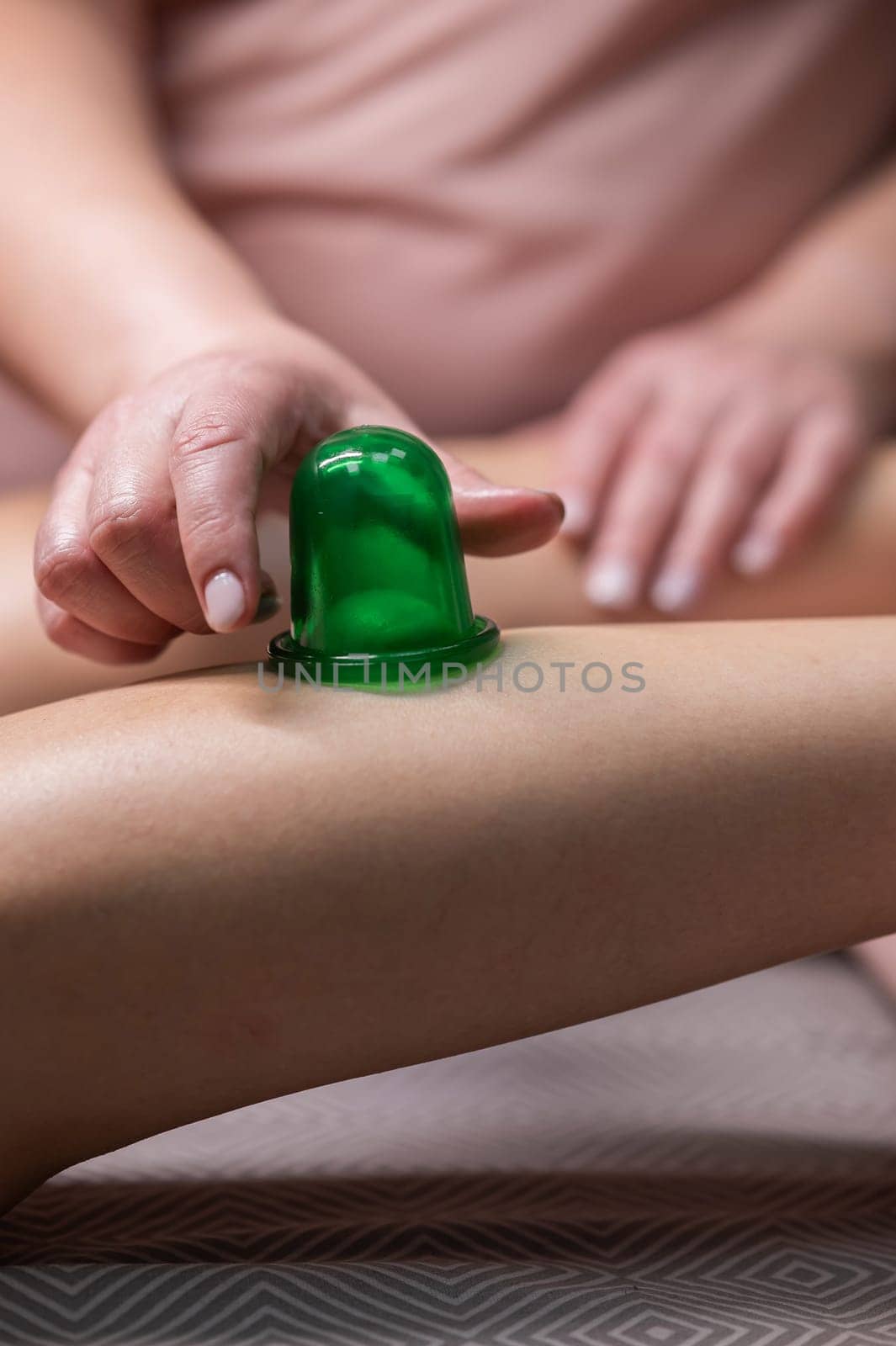 A massage therapist does a lymphatic drainage massage of the calf muscles with a vacuum plastic jar. Vertical photo. by mrwed54