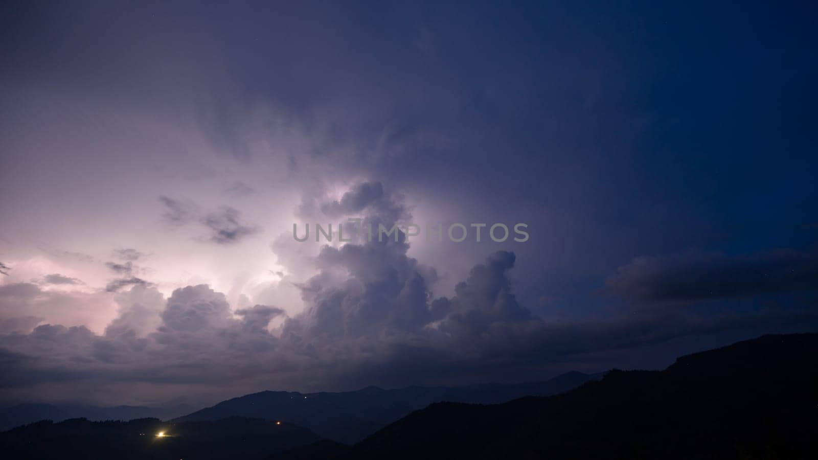 Evening thunderstorm with lightning in the mountains. Dramatic clouds during a thunderstorm pierce the light of lightning in a mountainous area. by Niko_Cingaryuk