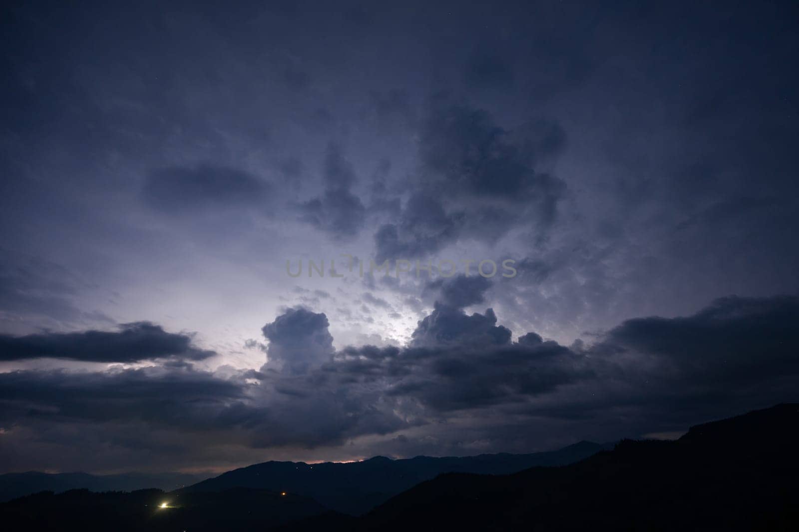 An evening thunderstorm with lightning in the Carpathian mountains, the village of Dzembronya. Dramatic clouds during a thunderstorm pierce the light of lightning in a mountainous area.