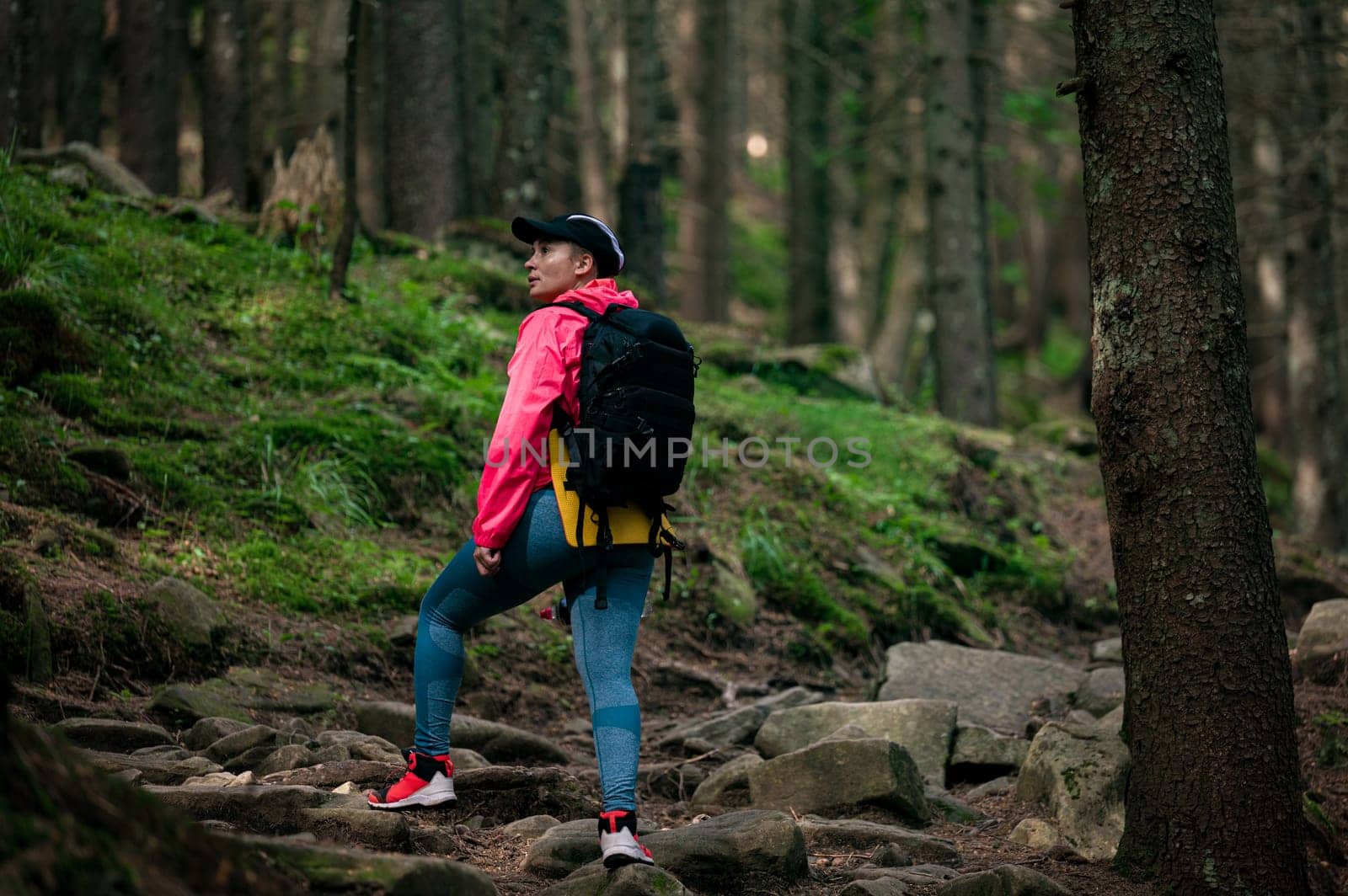 a girl in sportswear with a backpack on her shoulders and walks along a hiking trail in the forest, active recreation in the mountains.