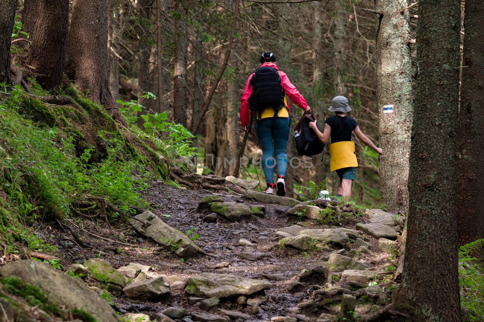 A mother and her son are walking along a mountain hiking trail with backpacks.