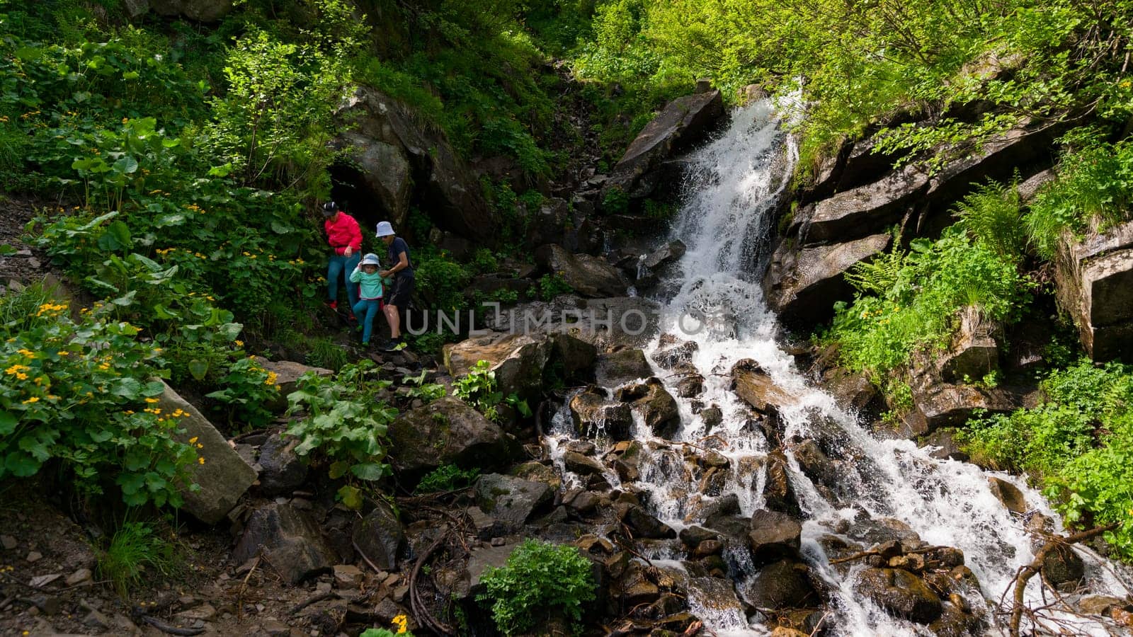 Mother and daughter are standing near a mountain waterfall, active summer vacation.