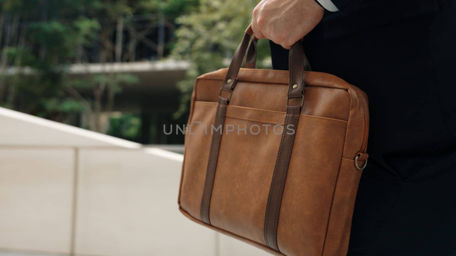 Close up of suitcase was held by profession businessman while project manager walking up stairs or step to new position at green eco city. Happy project manager using travel bag. Focus on bag. Urbane.