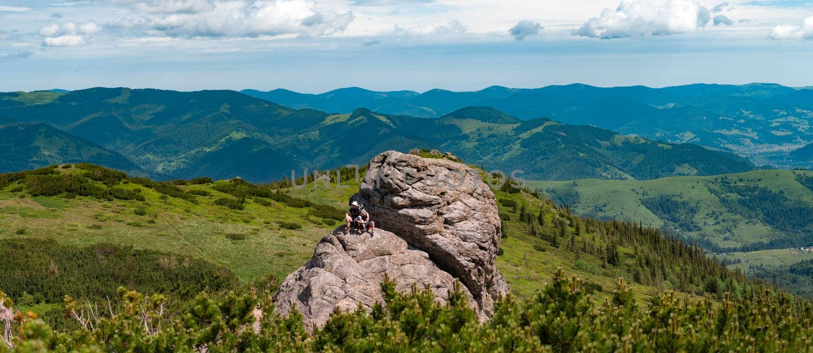 Dad and son are sitting on a big stone in the mountains, Vukhati Kamin mountain in the Carpathians of Ukraine, active recreation in the mountains in summer.