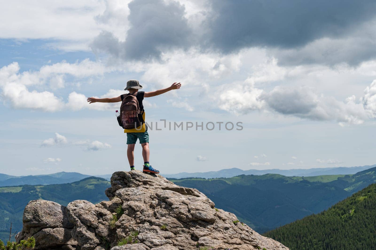 A schoolboy boy stands on a stone with his arms outstretched against the background of the Ukrainian Carpathians.