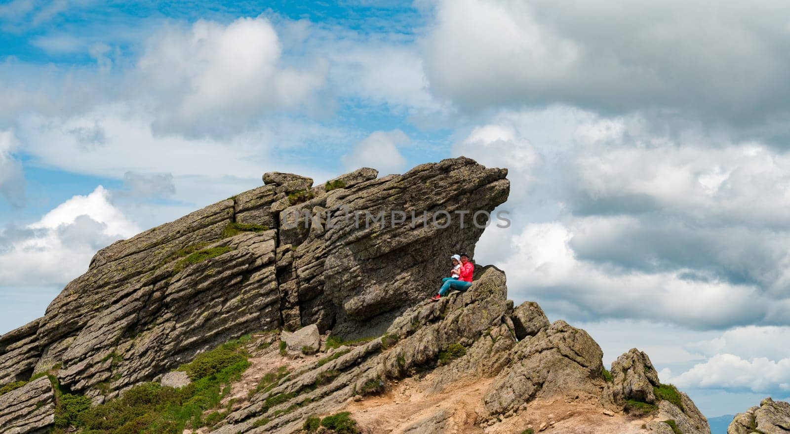 Mother and daughter are sitting on a rocky stone located on Mount Ukhaty Kamin, an eared stone in the Carpathians.