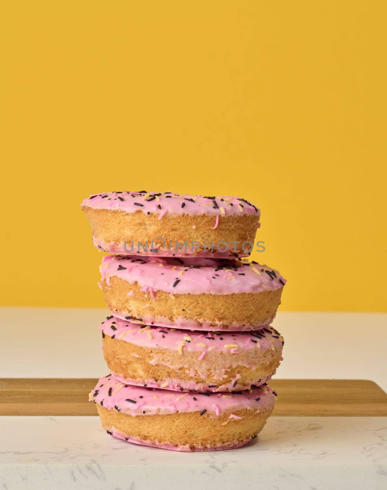 Donut covered with pink glaze and sprinkled with colorful sprinkles, yellow background by ndanko