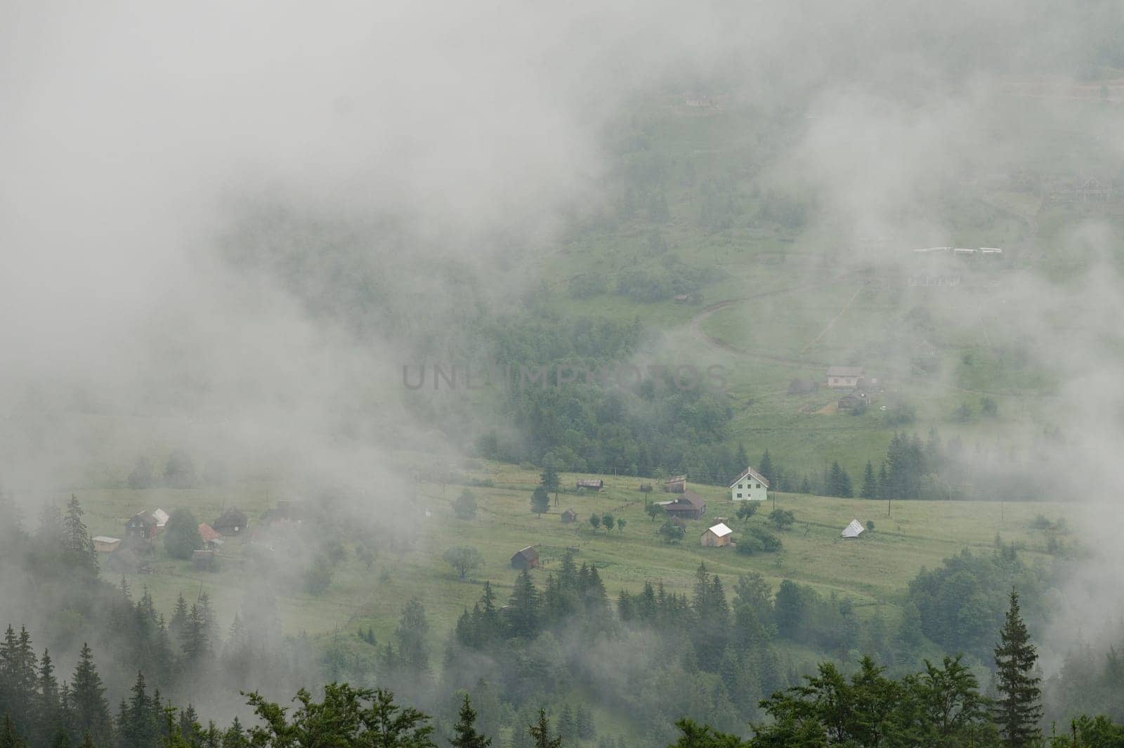 Dense fog in the mountains, through which houses and the village are barely visible, morning haze in the mountains.