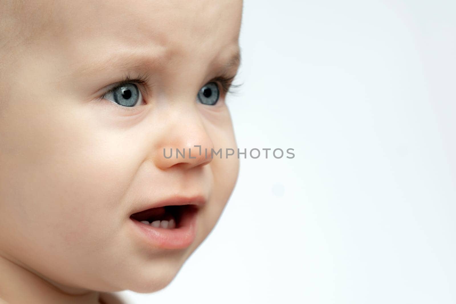 A baby with bright blue eyes is making a silly expression, with their mouth wide open