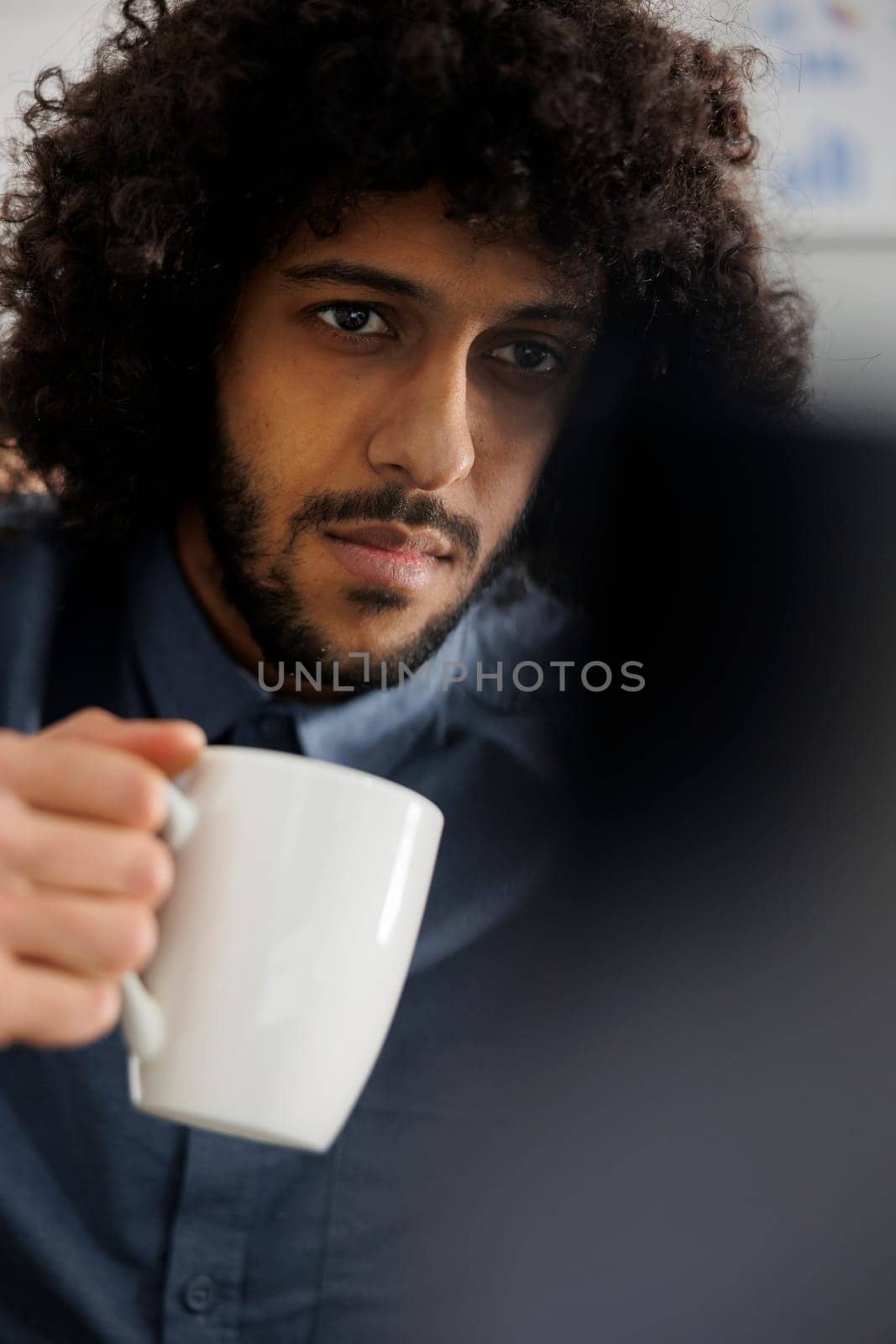 Start up company business employee drinking cofee and doing product management on laptop. Young arab entrepreneur holding tea cup and preparing marketing campaign on computer