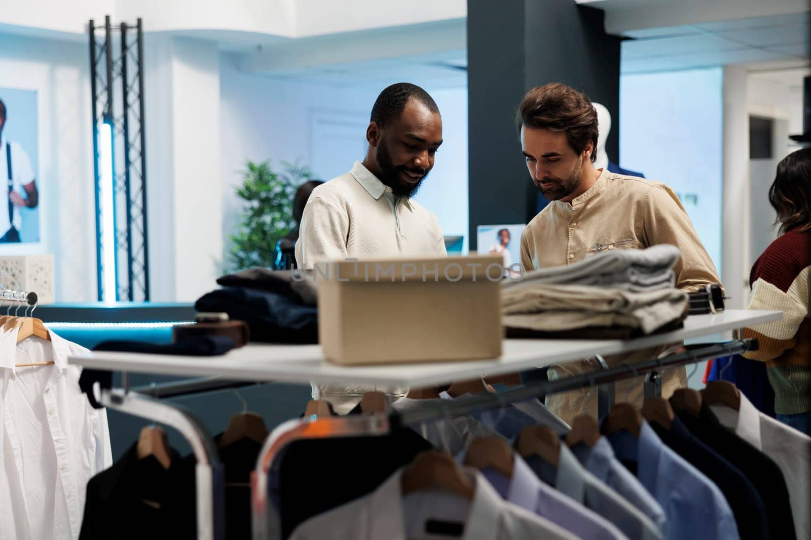 Clothing store assistant talking with african american customer, offering fashion advice. Fashion boutique providing consultation while exploring apparel rack with client