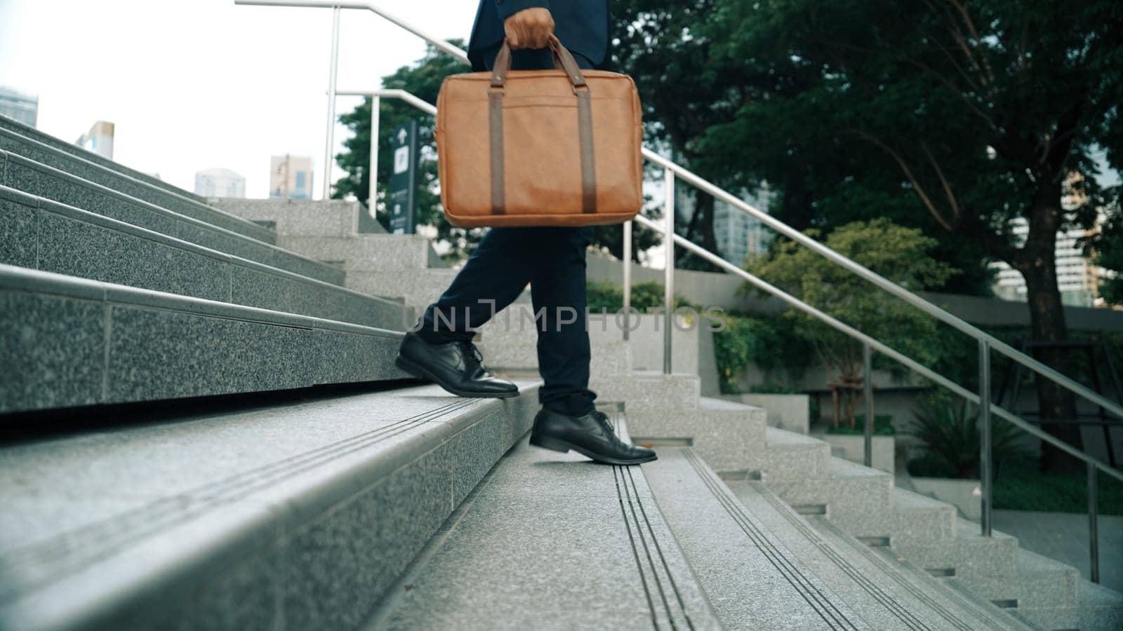 Closeup imaged of smart business man leg walking while holding a bag for working. Project manager going down to stairs for working. Represented transportation, traveling. Focus on leg. Exultant.