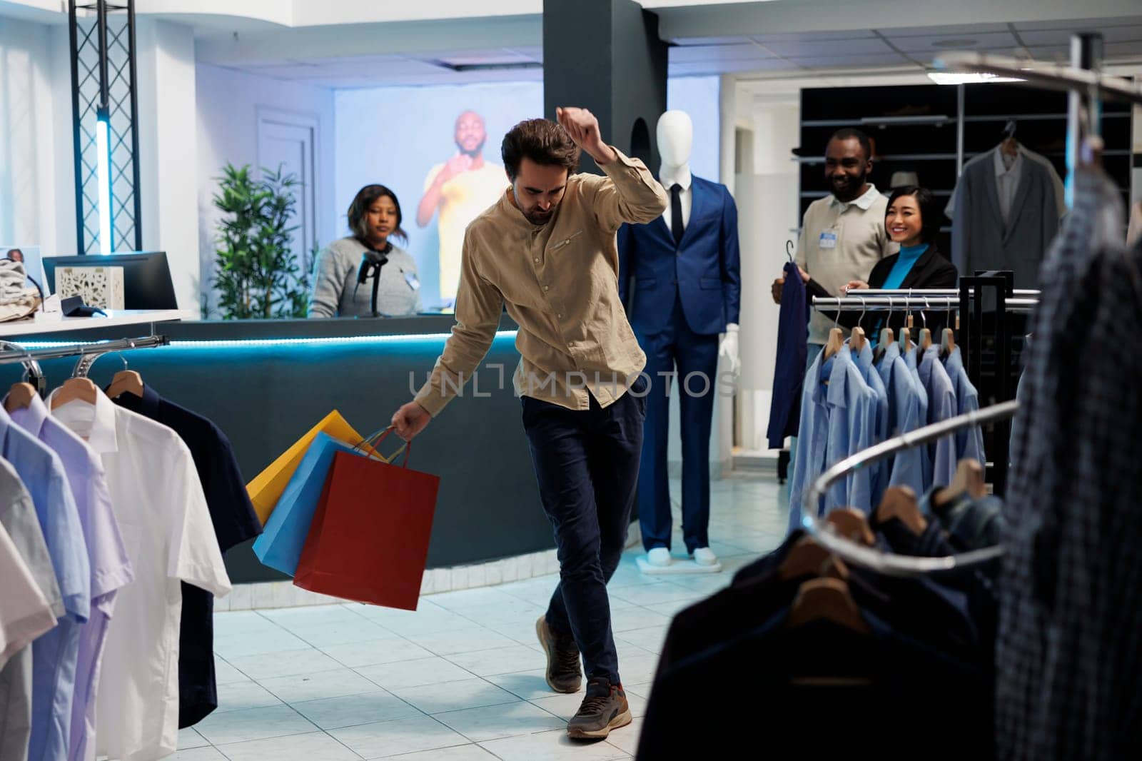 Cheerful man holding apparel purchase bags and dancing while shopping in clothing store. Department mall fashion boutique customer with packages making body moves to music