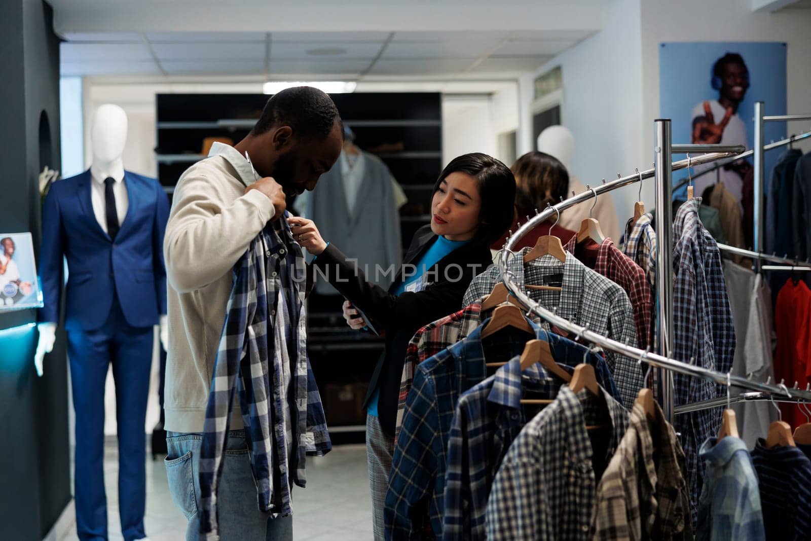 Boutique conslutant providing assistance in choosing casual clothes while customer trying on apparel. Shopping mall showroom worker offering help in selecting casual shirt