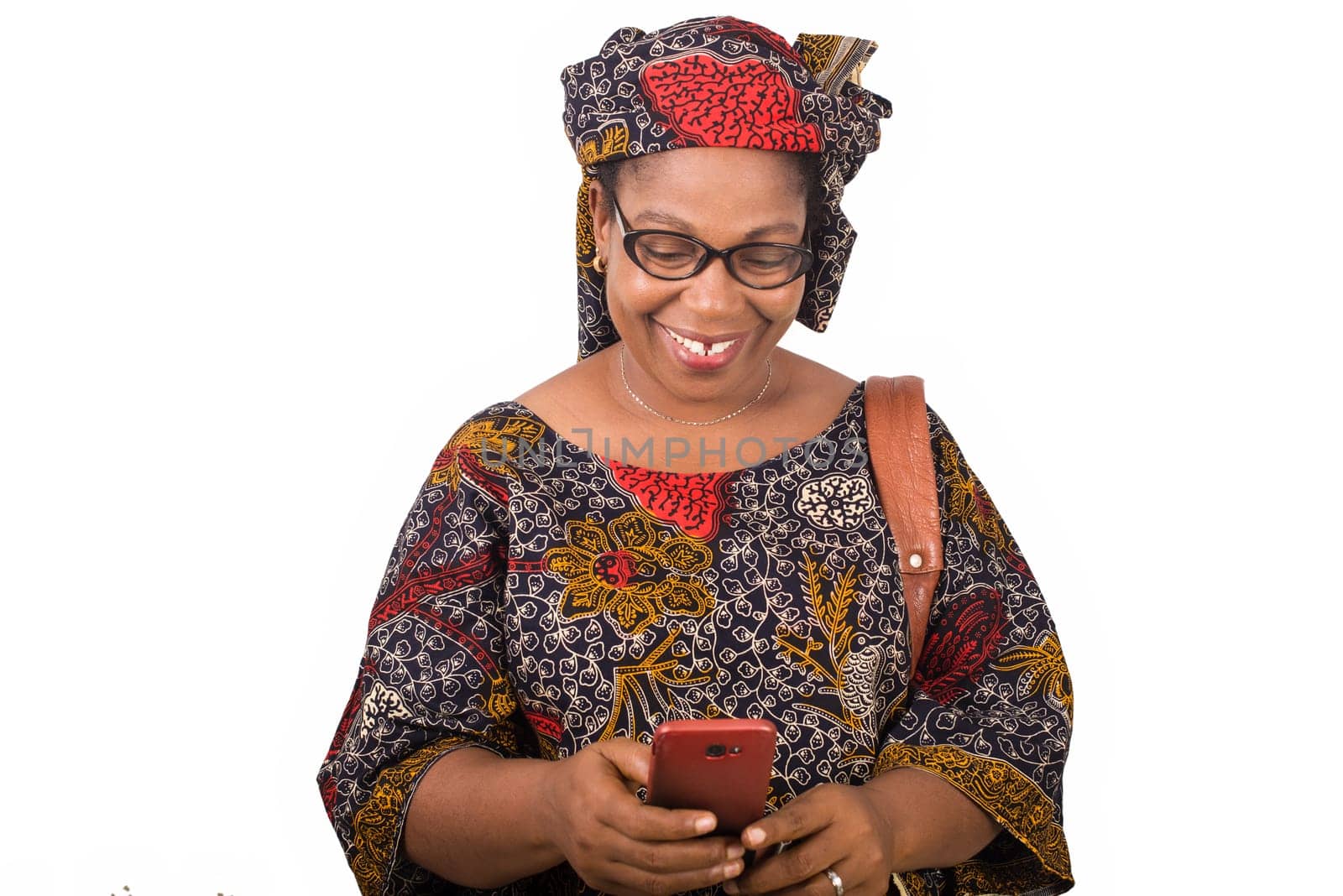 african mature woman in loincloth standing on white background looking at mobile phone while smiling.