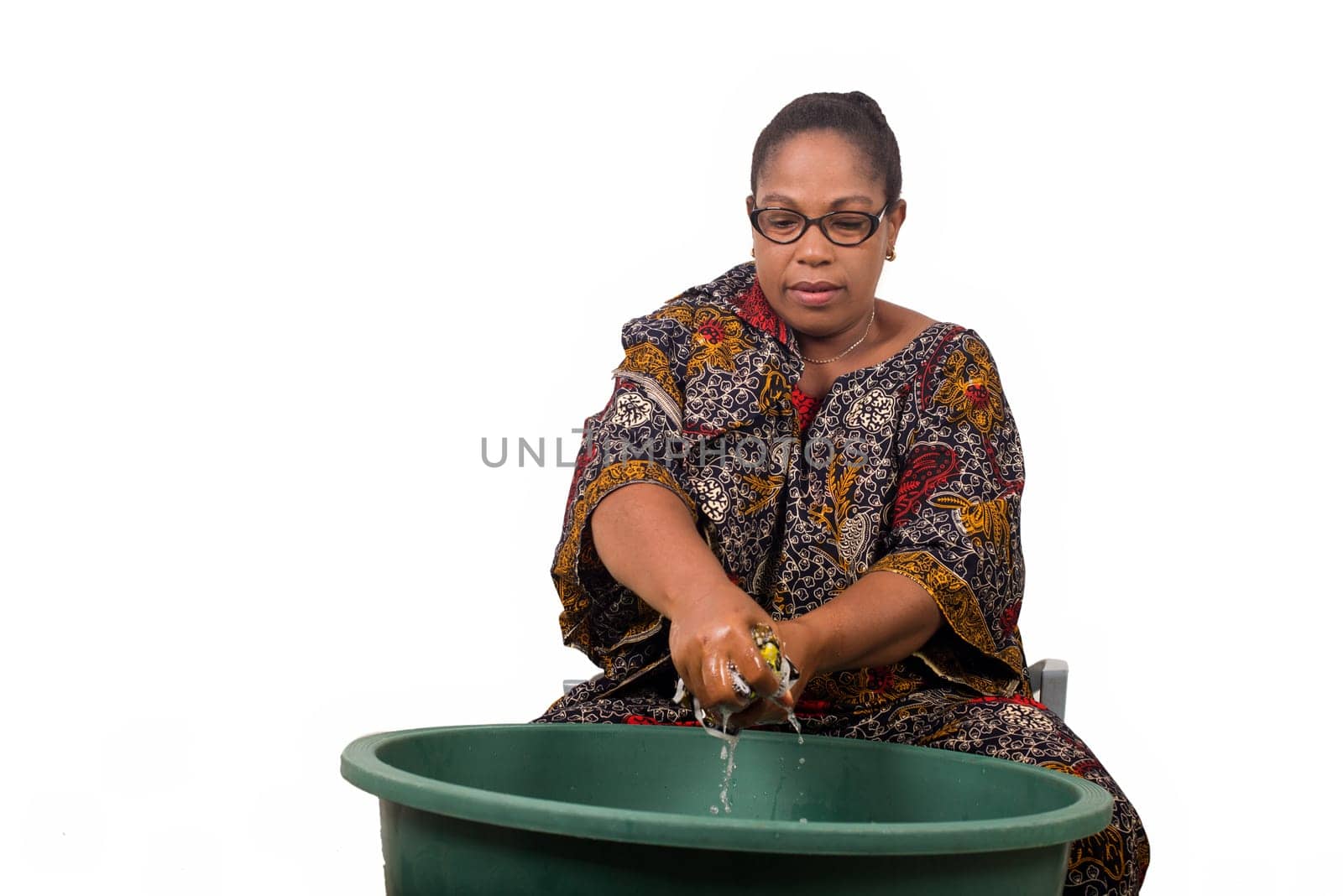 mature african woman in loincloth sitting doing laundry.