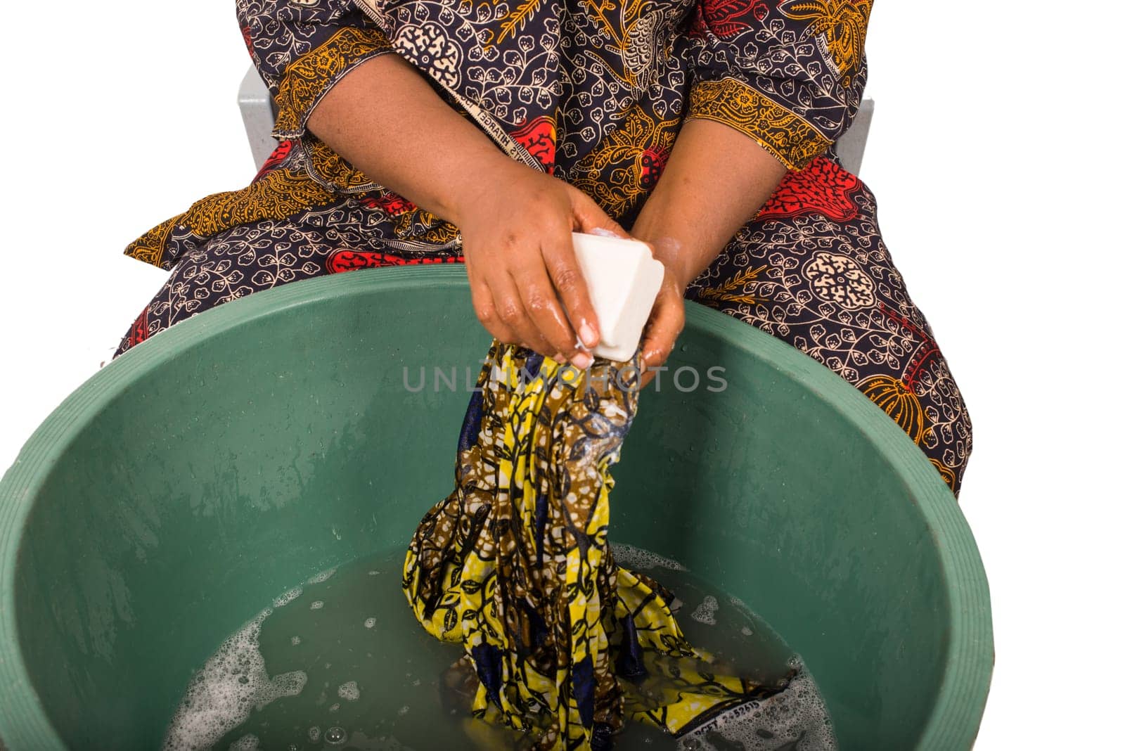 close up of woman's hands holding an African fabric that she is washing in a big green bowl with white soap