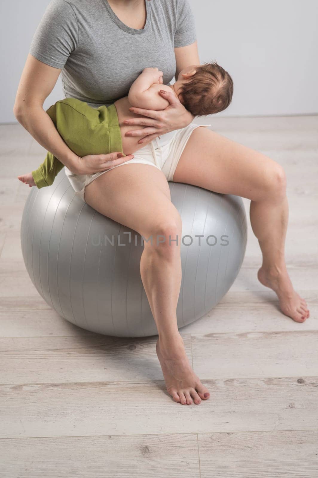 A faceless woman rocks her newborn son on a fitball. Vertical photo