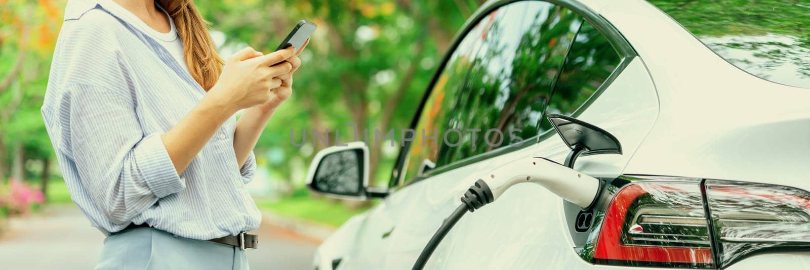 Young woman using smartphone to pay for electric car charging. Exalt by biancoblue