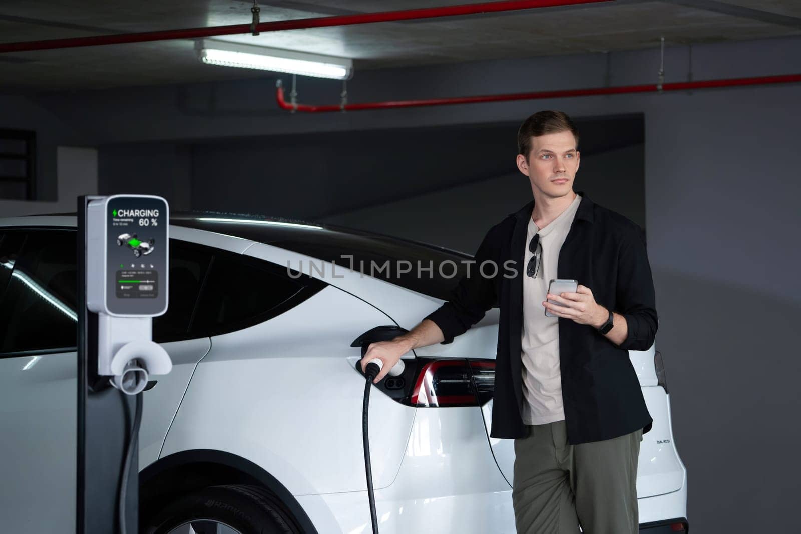 Young man travel with EV electric car to shopping center parking lot charging in downtown city showing urban sustainability lifestyle by green clean rechargeable energy of electric vehicle innards