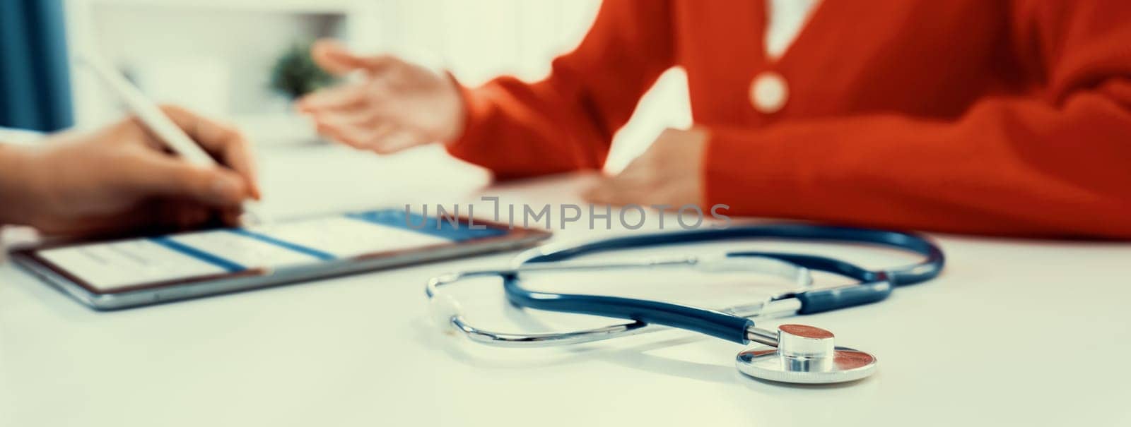 Focused stethoscope on office desk with blurred background of patient attending to doctor appointment at clinic or hospital discussing medical treatment or examining symptoms. Panorama Rigid