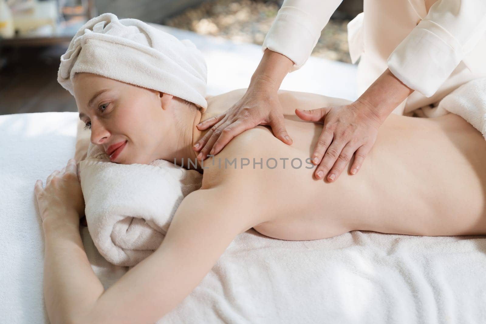 Beautiful young woman lies on spa bed during having back massage. Attractive caucasian woman having back massage at traditional spa salon, spa room . Relaxing and healthy concept Tranquility.