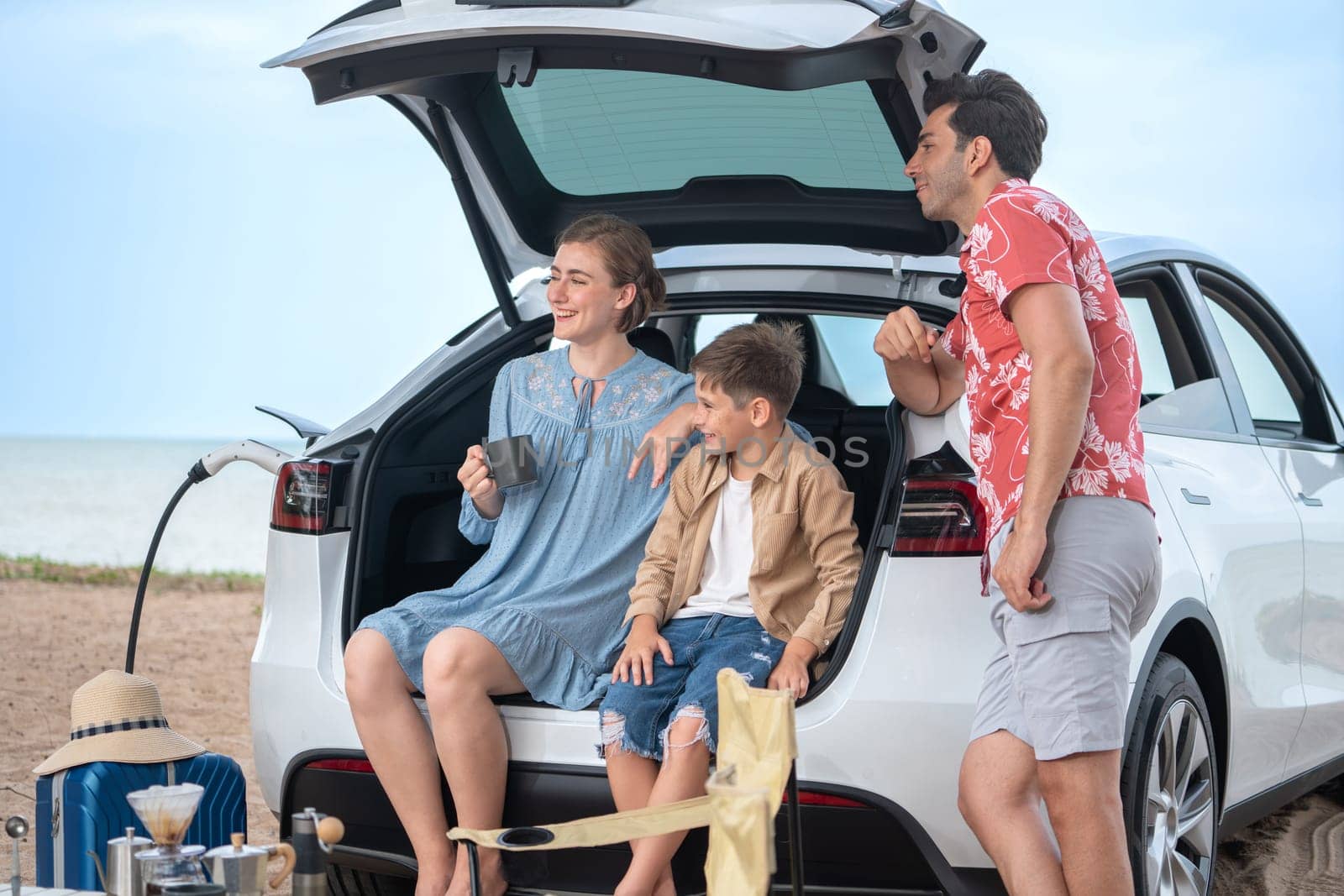 Family vacation trip traveling by the beach with electric car, happy family recharge EV car, enjoying outdoor camping coffee. Seascape travel and eco-friendly car for clean environment. Perpetual