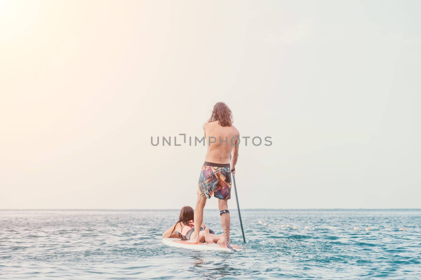 Sea woman and man on sup. Silhouette of happy young woman and man, surfing on SUP board, confident paddling through water surface. Idyllic sunset. Active lifestyle at sea or river