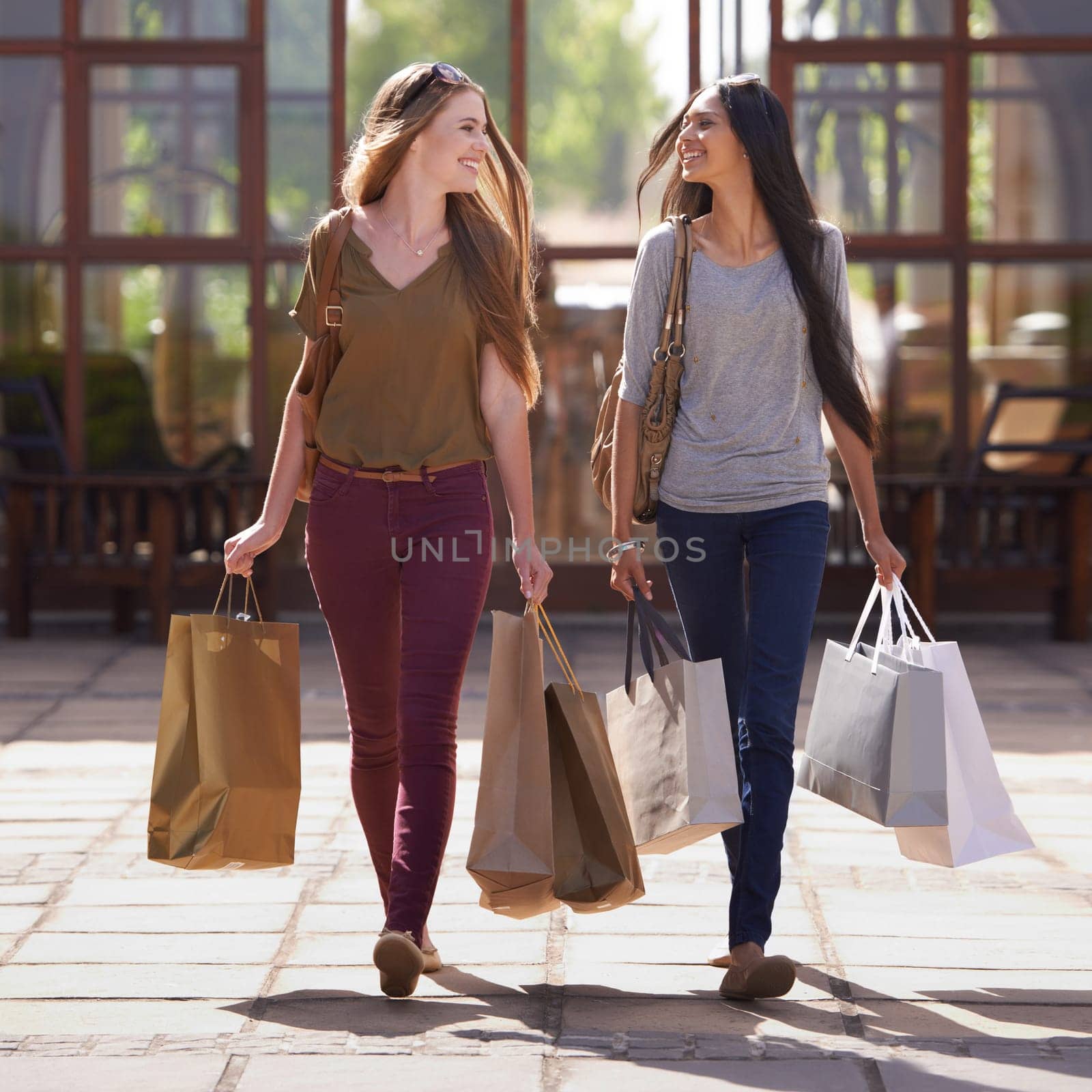 Women, friends and walking with shopping bag or talking of fashion, sale and discount outdoor by store, mall or city. Young and happy people with style, clothes and luxury for commerce or retail by YuriArcurs