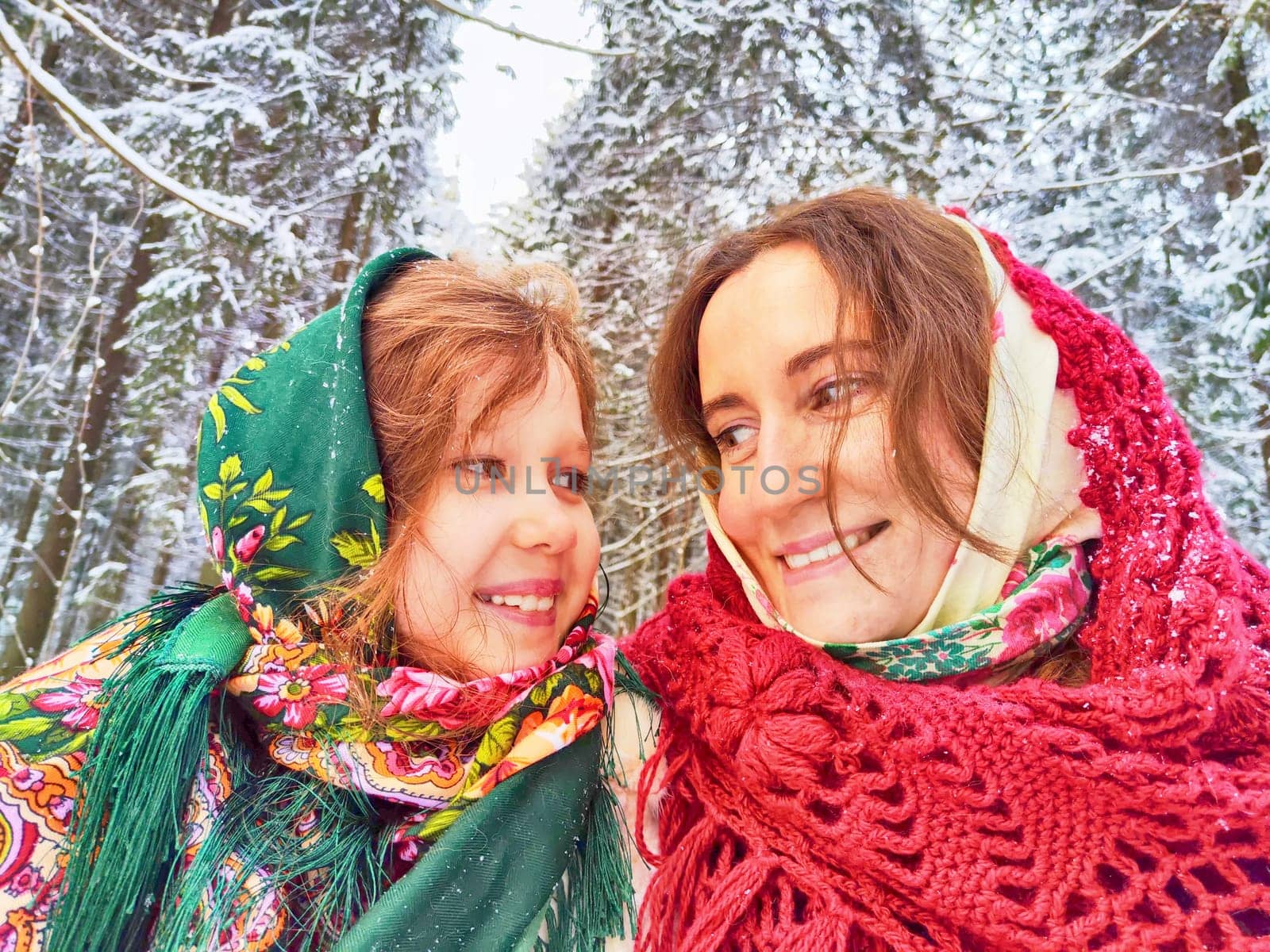 Portrait of happy family. Mother and daughter in shawls in winter forest. Ethnic clothes for carnival Maslenitsa