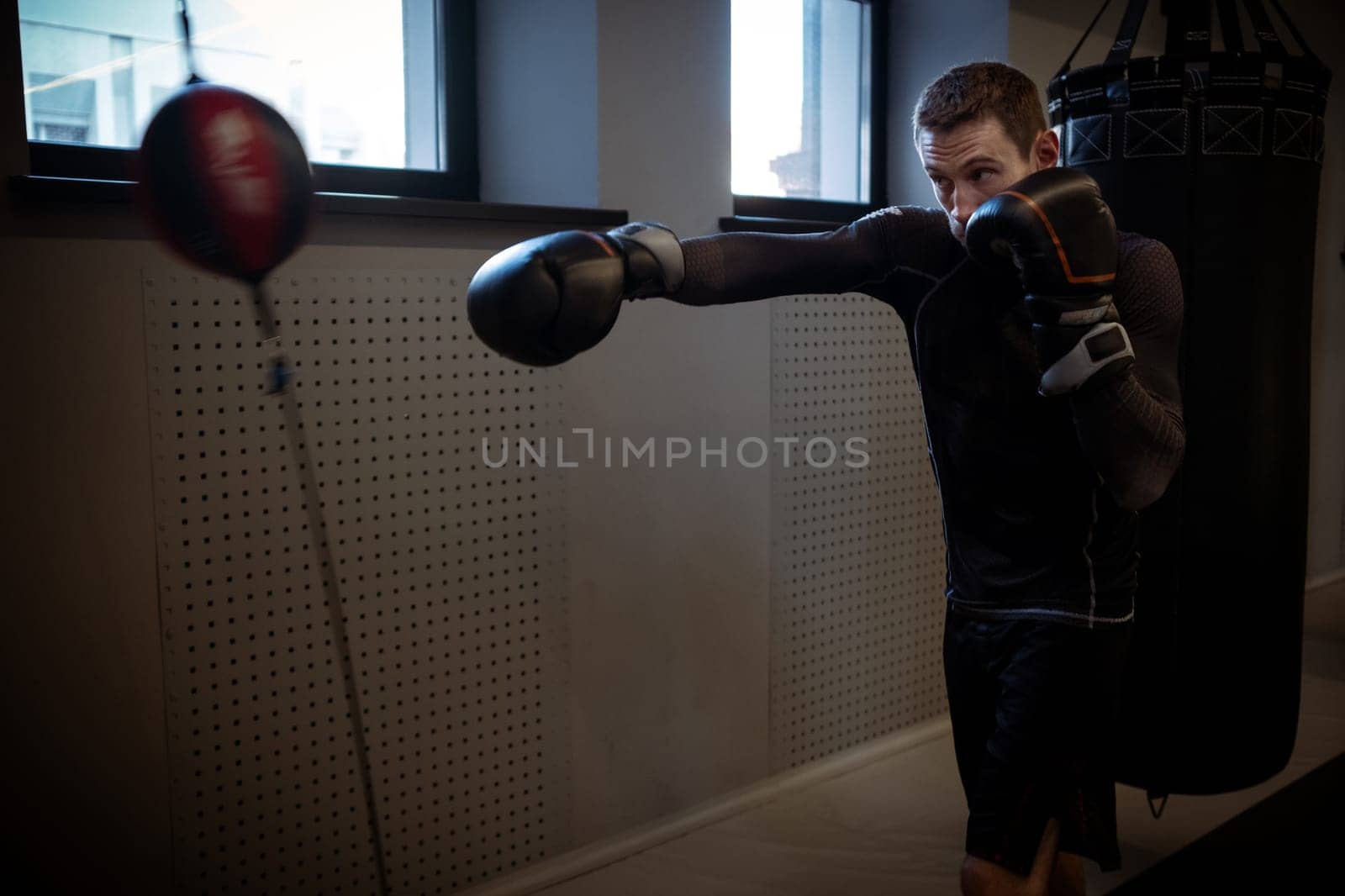 Motivated young adult mixed martial artist sharpening accuracy and timing using double-end bag at modern boxing gym, demonstrating focus and technique