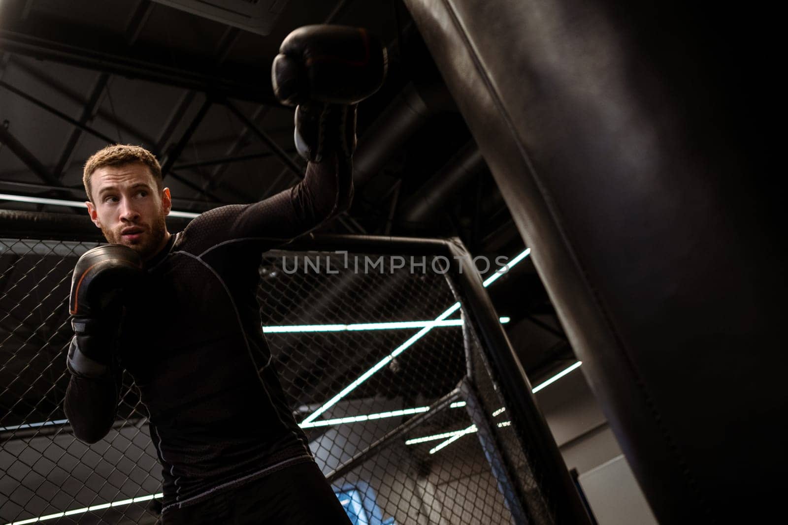 Focused athlete in boxing gloves working on punching technique and power on heavy bag during training session in gym