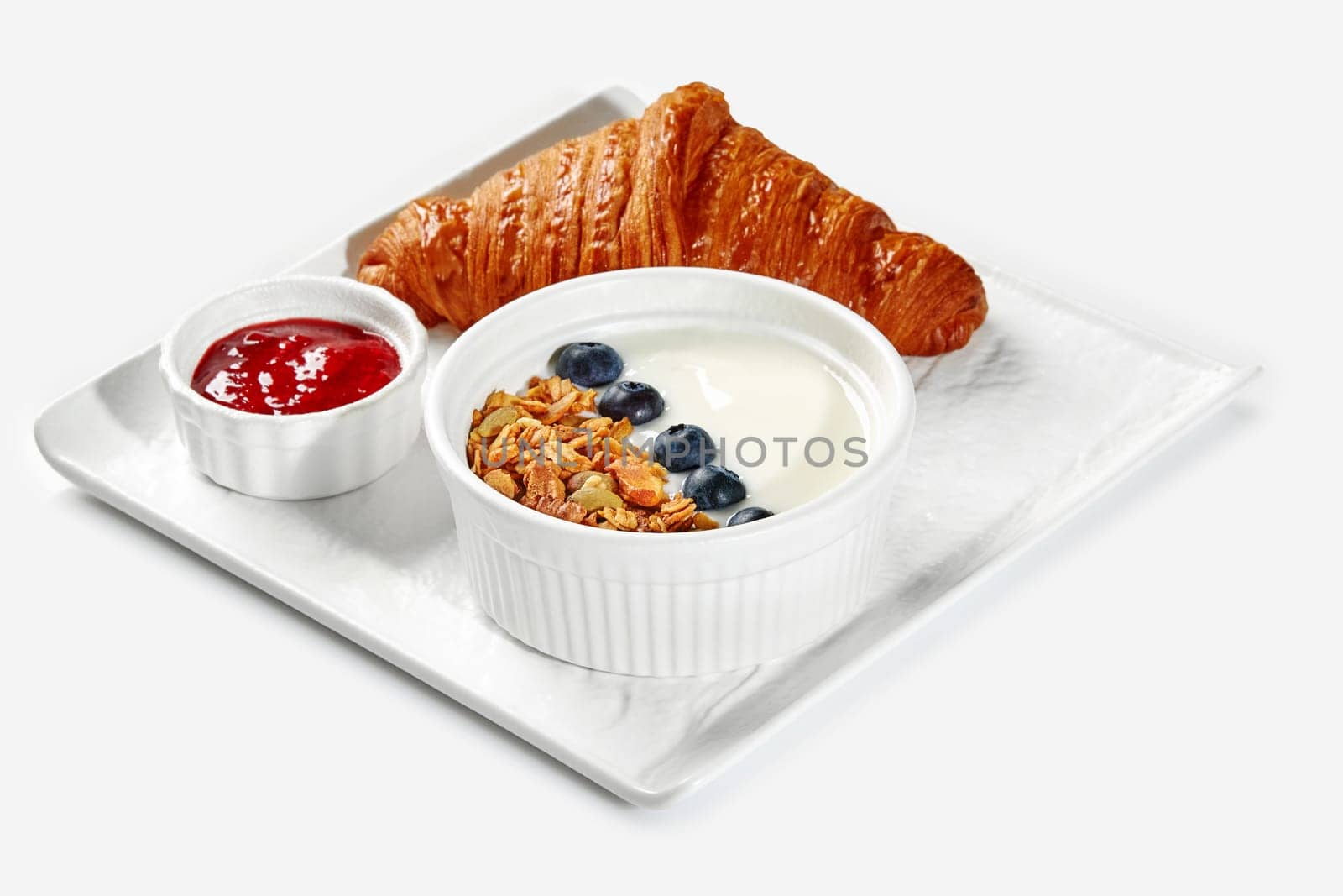 Classic flaky French croissant, smooth yogurt with granola and fresh blueberries, and homemade berry compote served as breakfast on white tray