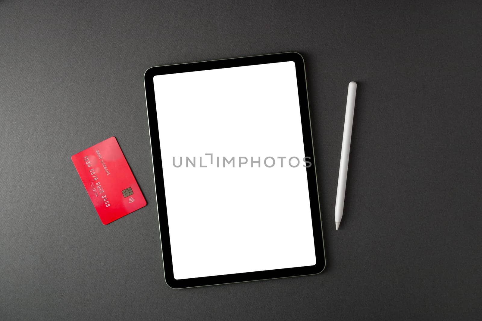 Credit card lying on tablet with blank screen on dark gray table by Sonat