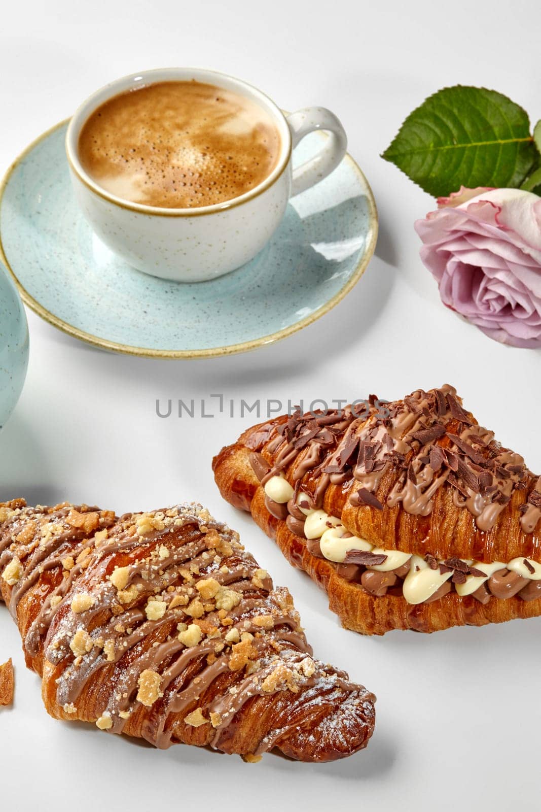 Croissants filled with dark and white chocolate custard garnished with shavings and caramelized crumbs, served in romantic setting with freshly brewed cup of espresso and blooming rose