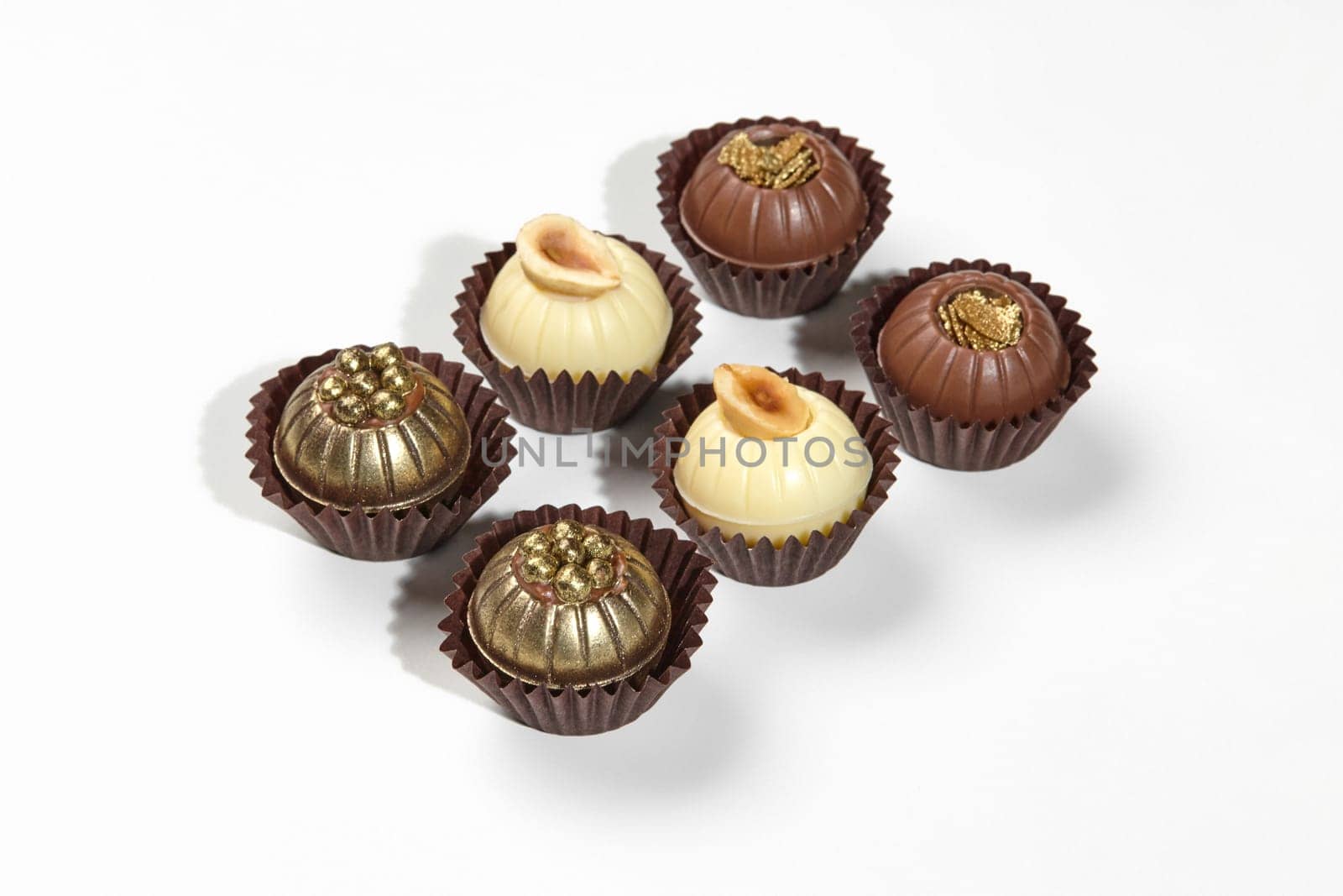 Designer exquisite chocolate candies in shape of balls decorated with hazelnuts, caramel crumbs and golden pearls, isolated on white background