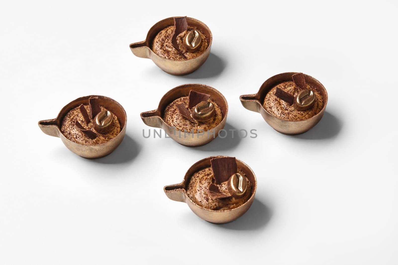 Handmade chocolate sweets with rich coffee cream, artistically designed to look like small coffee cups, against white backdrop
