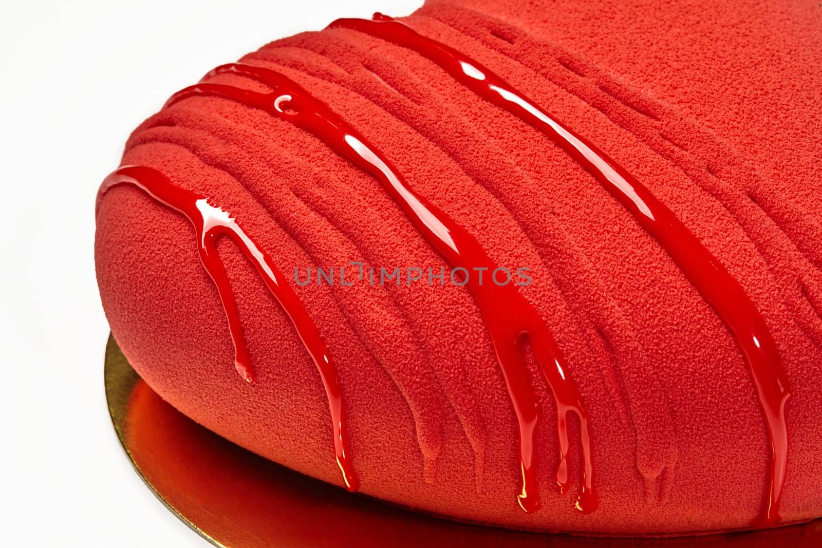 Closeup of velvet texture of vibrant red heart-shaped cake topped with glossy icing on gold cardboard, isolated on white background. Romantic delicious gift for Valentines Day