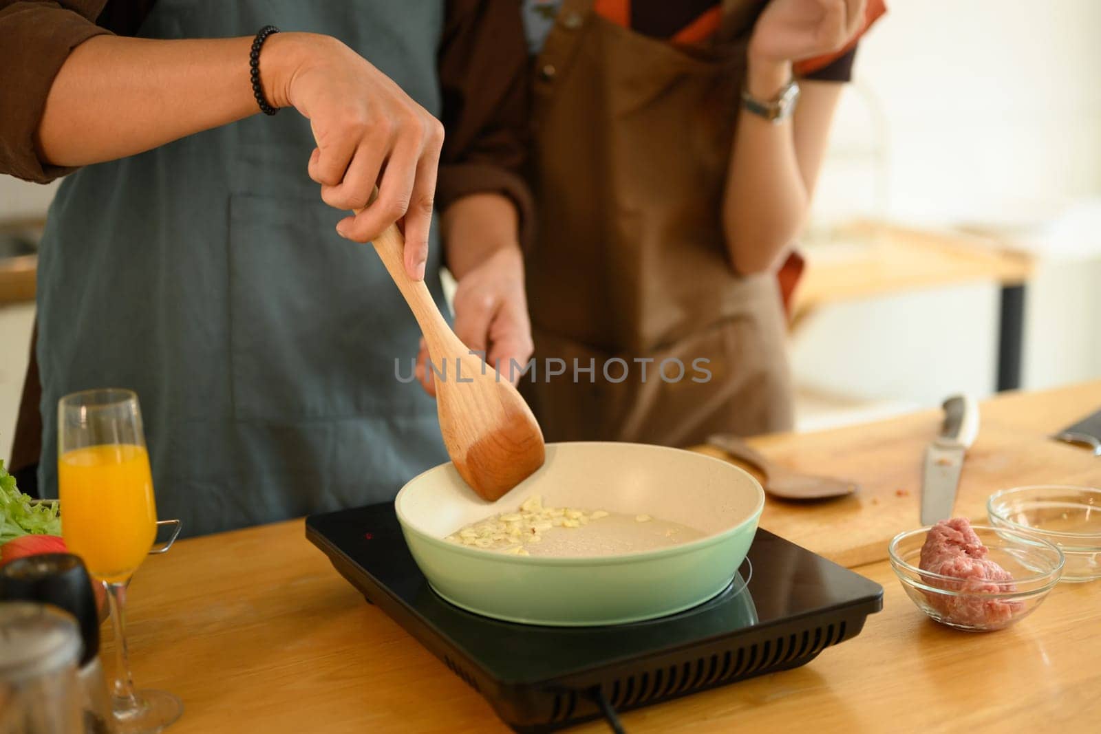 Man wearing apron sauteing garlic in the frying pan, cooking with his wife in the kitchen.