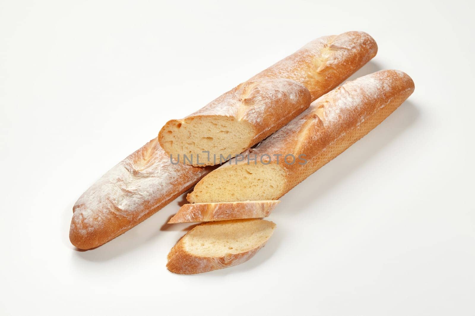 Two whole and sliced fresh French baguettes with golden crust and airy texture, isolated on white background. Traditional bakery products concept